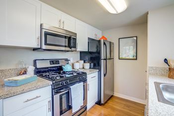 Model home kitchen with dishwasher, gas stove, refrigerator, granite countertops and hardwood inspired flooring at Addison Ranch Apartments, Petaluma
